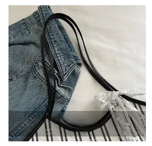 Detail of washed denim tote with black leather handle and delicate white lace bow