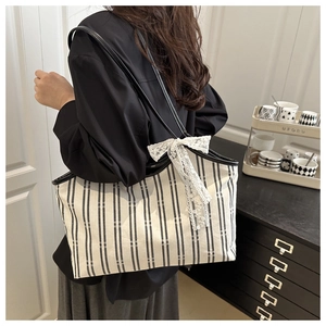 Detail of striped canvas tote bag featuring a white lace bow and spacious interior design