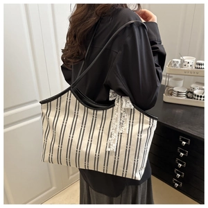 Detail of striped canvas tote bag featuring delicate white lace bow and black leather strap