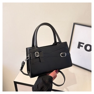 Detail view of black handbag featuring a silver buckle and bow knot decorative strap