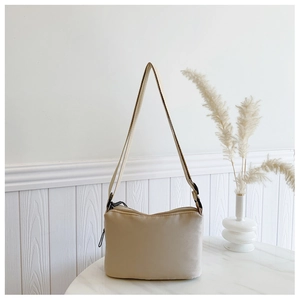 Close-up of the beige shoulder bag zipper and adjustable strap on a marble surface