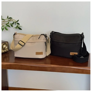 Detail of nylon crossbody bags in cream and black with adjustable wide straps on wood table