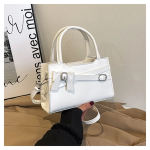 Detail of white leather handbag featuring decorative bow and gold metal buckle accents