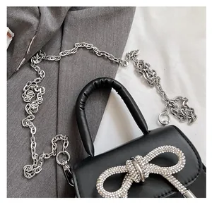 Detail of a black mini bag showing the sparkling rhinestone bow and silver chain strap