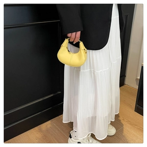 Mini yellow crescent bag held by model featuring gold metal ring handle and PU leather