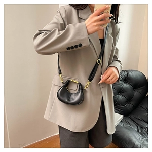 Detail of black semi-circle leather bag with golden hardware on grey blazer outfit
