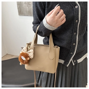 Detail of khaki pebbled leather bucket bag with cute plush monster charm and embossed text