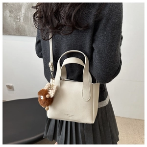 Detail of cream white leather bucket bag with brown pompom and embossed logo