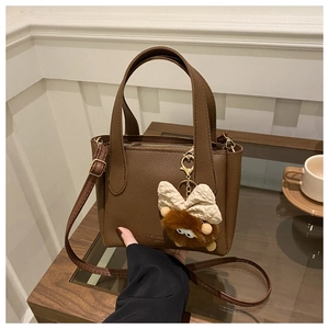 Détail du sac seau en cuir grainé marron avec une breloque de monstre en peluche