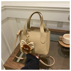 Détail du sac à main beige motif litchi avec breloque en peluche dans un décor de café
