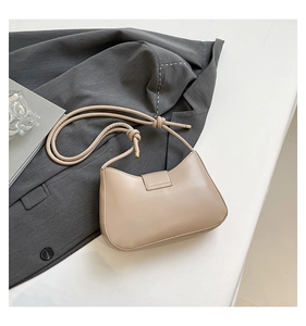 Detail of light beige crescent shoulder bag with knotted strap and metal hardware