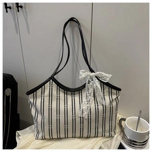 Detail of striped canvas tote bag featuring a white lace bow and black handle contrast