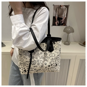 Detail of a woven tote bag with artistic black graffiti patterns and black leather straps