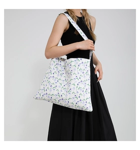 Detalle del bolso tote de lona blanca con flores moradas llevado por una modelo