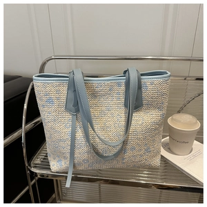 Detailed close-up of woven tote bag featuring light blue leather straps and floral texture