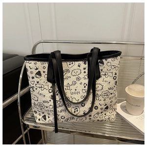 Detail of woven tote bag with artistic black graffiti and leather handles on display