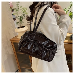 Deep brown glossy shoulder bag with bow details worn by a model in a minimalist interior