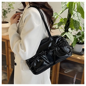 Detail of glossy black pleated shoulder bag showing premium faux leather texture on model