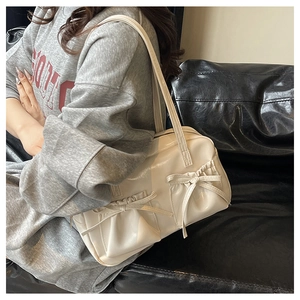 Detail view of a cream pleated shoulder bag with decorative ribbons on a gray hoodie