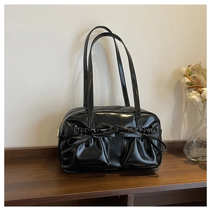 Close-up of black glossy leather shoulder bag with decorative bow ties and twin front pockets