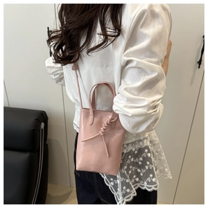 Détail du sac seau en cuir verni rose clair avec poignée nouée et logo en relief