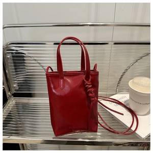 Detail of red leather mini tote bag with embossed fashion text and long shoulder strap