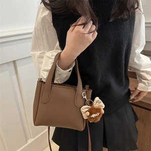Brown litchi leather bucket bag with top handles and cute plush monster charm