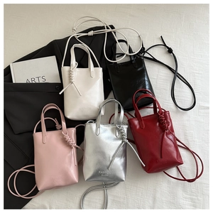 Flat lay of mini tote bags in five colors with cross-body straps and woven knot detail