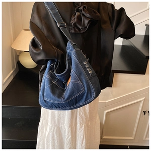 Dettaglio della borsa a mezzaluna in denim blu scuro con cuciture bianche e tasca sfrangiata