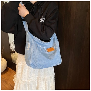 Dettaglio borsa tote in denim azzurro con etichetta in pelle arancione su una modella