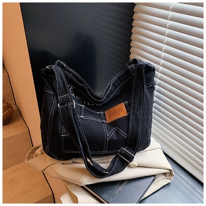 Detail of black denim tote bag featuring white contrast stitching and a leather patch