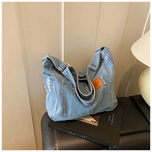 Detail of light blue denim tote with W-shaped decorative stitching and embossed logo tag