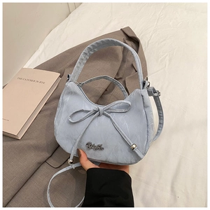 Detail of light blue bow handbag with textured fabric and metallic logo on white bedding