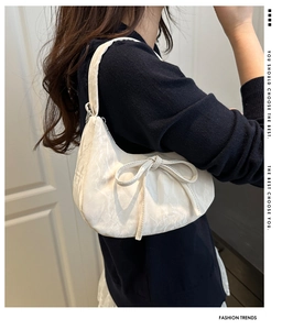 Detail showing textured cream shoulder bag with minimalist bow decoration on shoulder