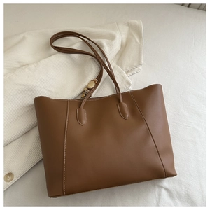 Brown leather tote bag featuring white contrast stitching and a silk scarf on the handle