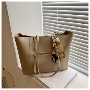 Detail of beige tote bag with elegant floral scarf on handle and front zipper pocket