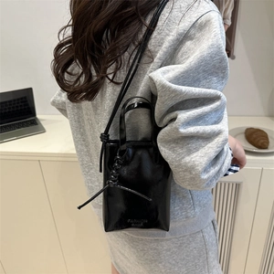 Minimalist black glossy leather tote bag with knotted strap shown in a lifestyle setting