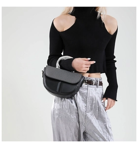 Detail of black saddle bag featuring signature T-shaped hardware and metallic handle