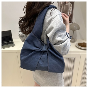 Blue denim shoulder bag with a large bow detail shown on a model in a cozy home setting