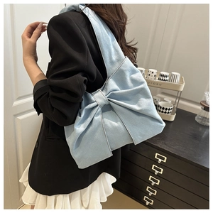 Detail of light blue denim shoulder bag featuring a large bow design worn by a model
