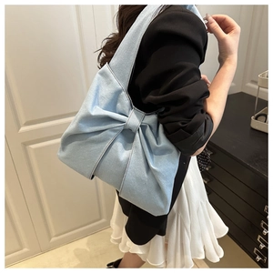 Close-up of light blue denim tote bag with a large bow detail worn on the shoulder