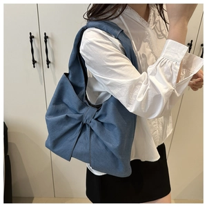 Blue denim shoulder tote bag with a large decorative bow on model in home setting