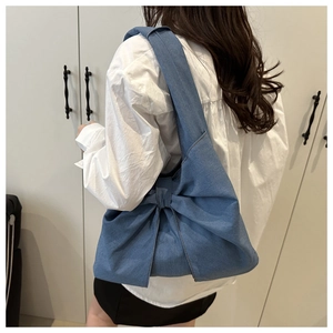 Detail of the large denim bow knot design on the side of a blue shoulder bag