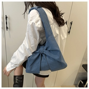 Detail of blue denim tote bag featuring a large decorative bow and textured fabric