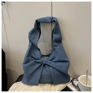 Detail of blue denim tote bag featuring a large bow design on a soft silk background