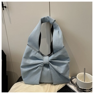 Detail of light blue denim tote bag with a large decorative 3D bow and wide handle