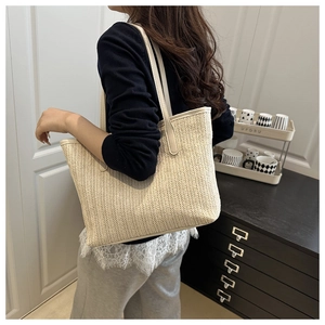 Detail of herringbone weave texture and beige leather straps on a large straw tote bag