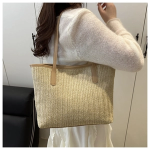 Close-up of woven straw tote bag with brown leather handles worn by a female model