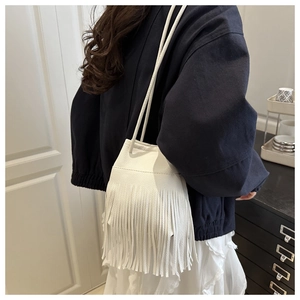 White pebbled leather bucket bag with long fringe tassels shown on shoulder
