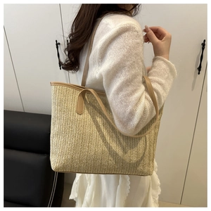 Side view of a large woven straw tote bag with beige herringbone pattern and brown handles